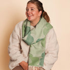 Woman wearing a green patterned scarf and white coat against a beige background