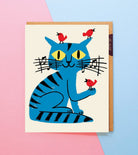 Card with a blue cat illustration and red birds on a pink and blue background