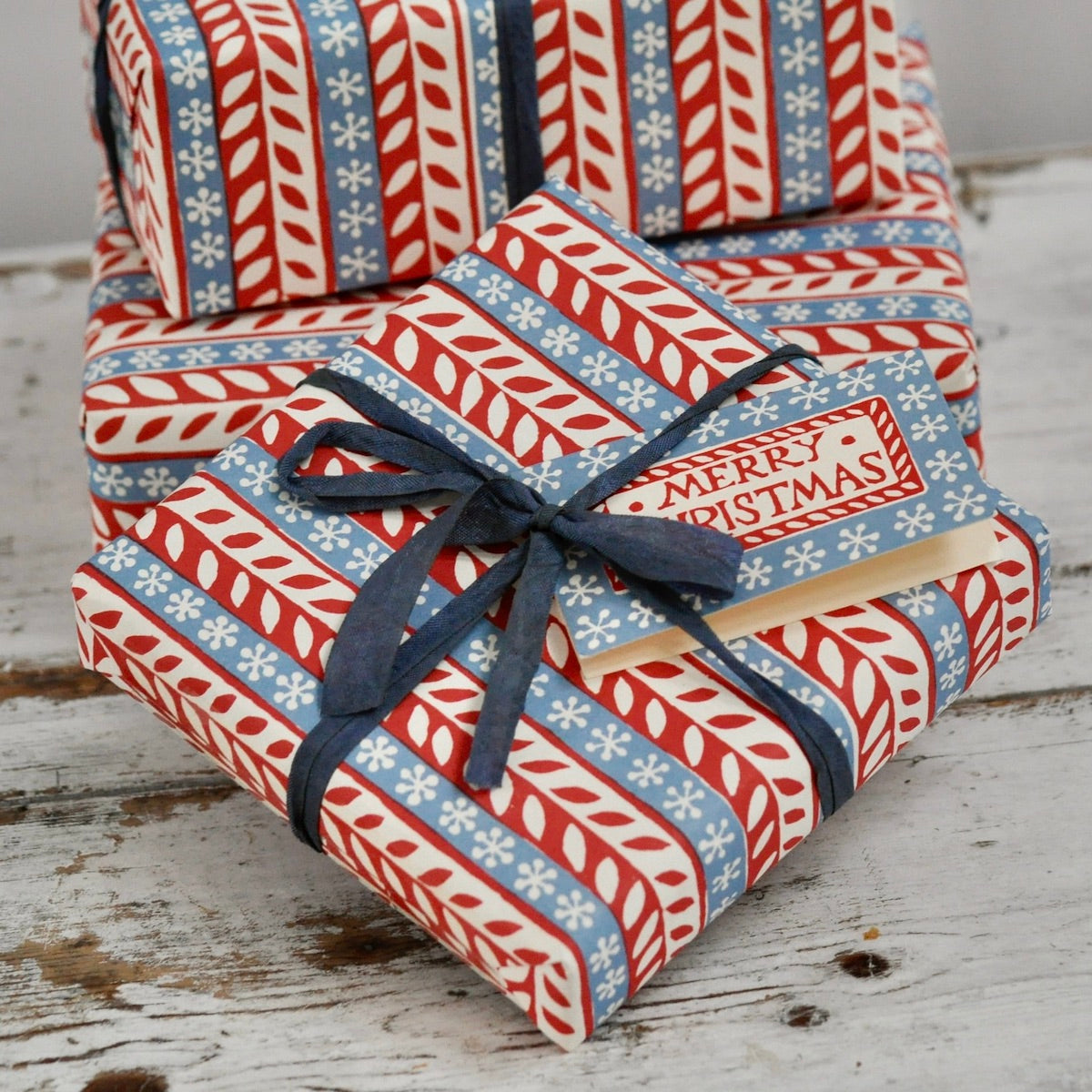 Stack of Christmas-themed gift boxes with a blue ribbon on a wooden surface