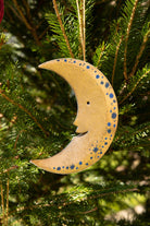 Wooden crescent moon ornament with blue star patterns hanging on a Christmas tree.