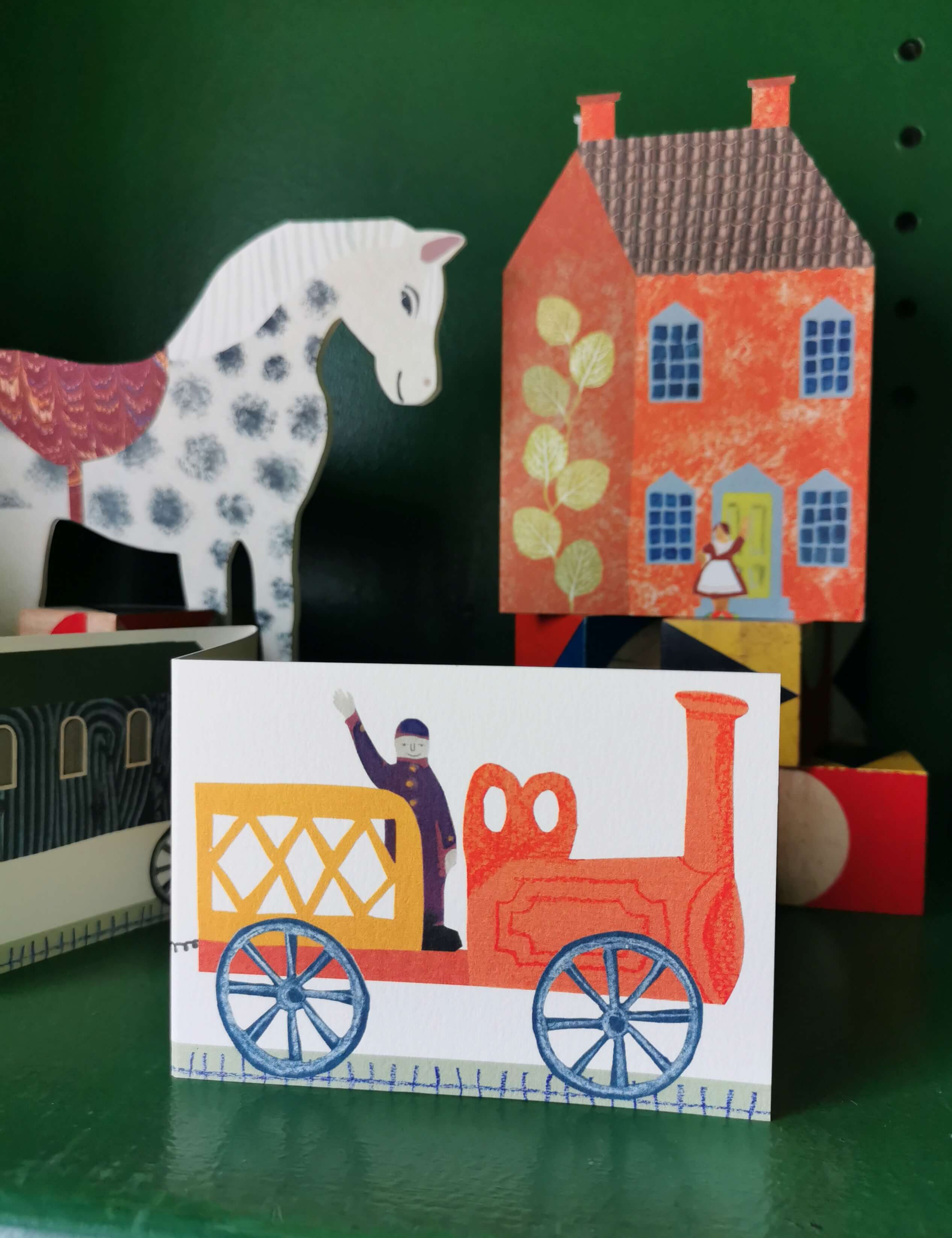 Colorful toy train card with a horse and house in the background