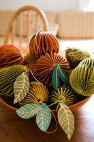 Decorative paper balls with leaf patterns in a bowl on a wooden surface