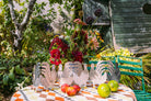 Decorative paper chickens on a table with apples and limes, set against a garden backdrop.