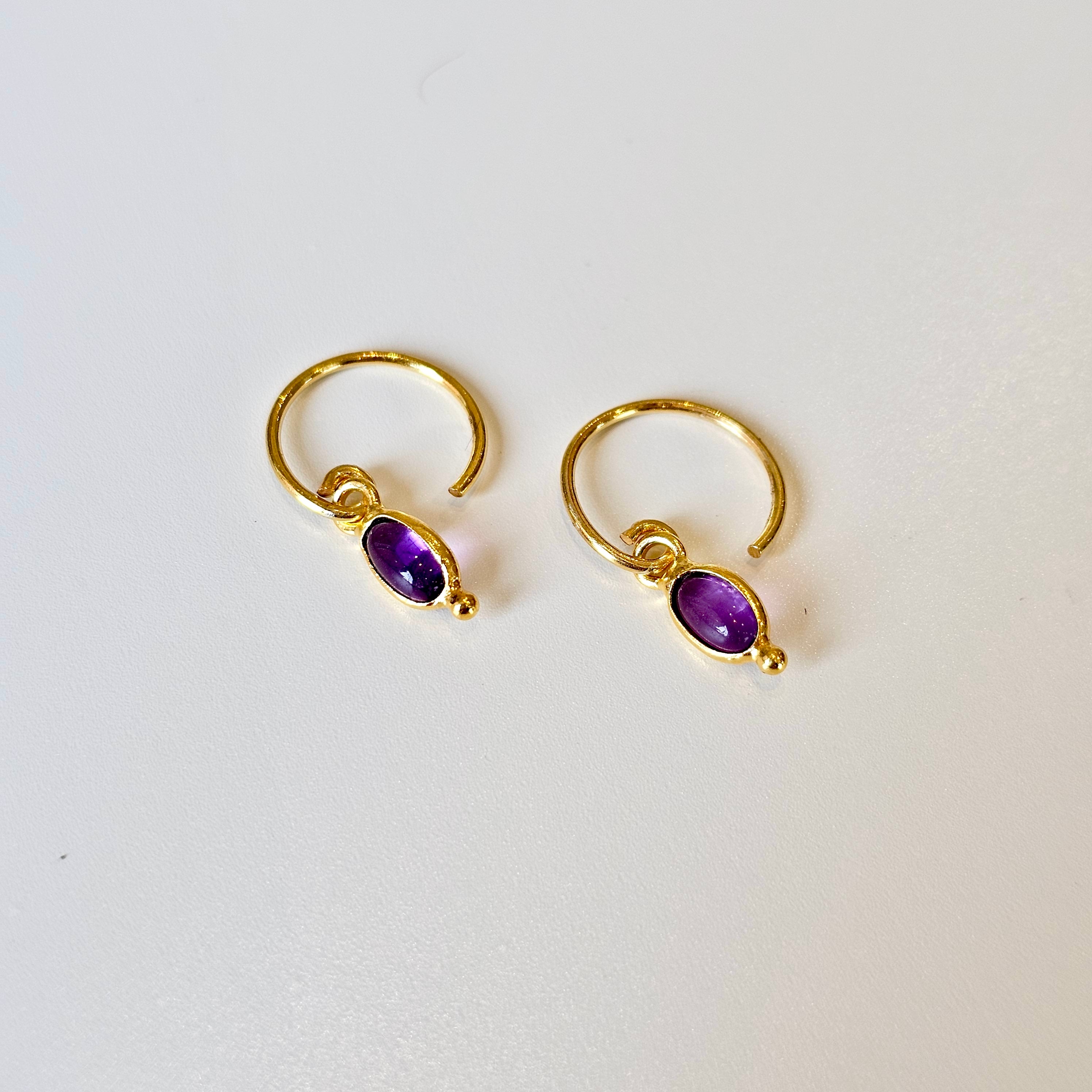 Gold hoop earrings with amethyst gemstones on a white background
