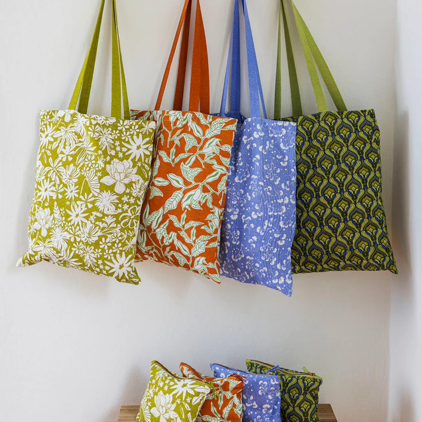 Colourful patterned bags hanging on a wall rack with additional bags on a wooden stool below.