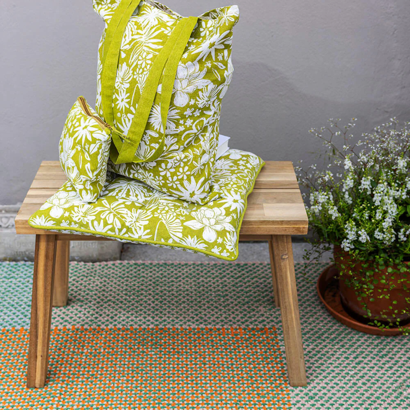 Green floral bag on a wooden chair with a grey wall and plant in the background