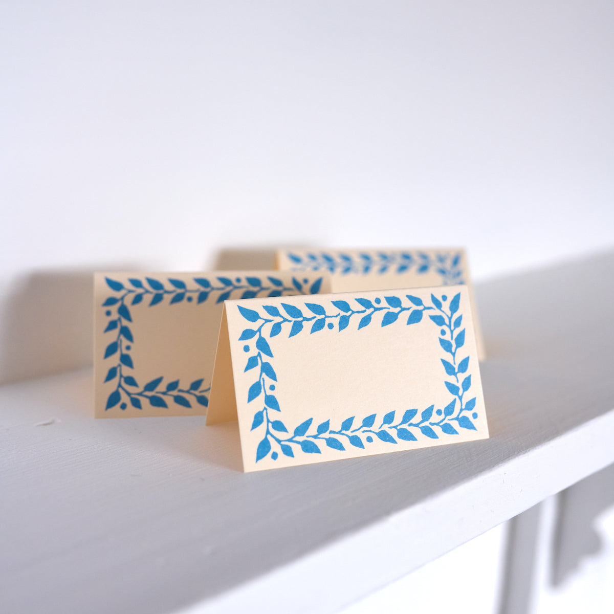 Two beige cards with blue leaf patterns on a white surface