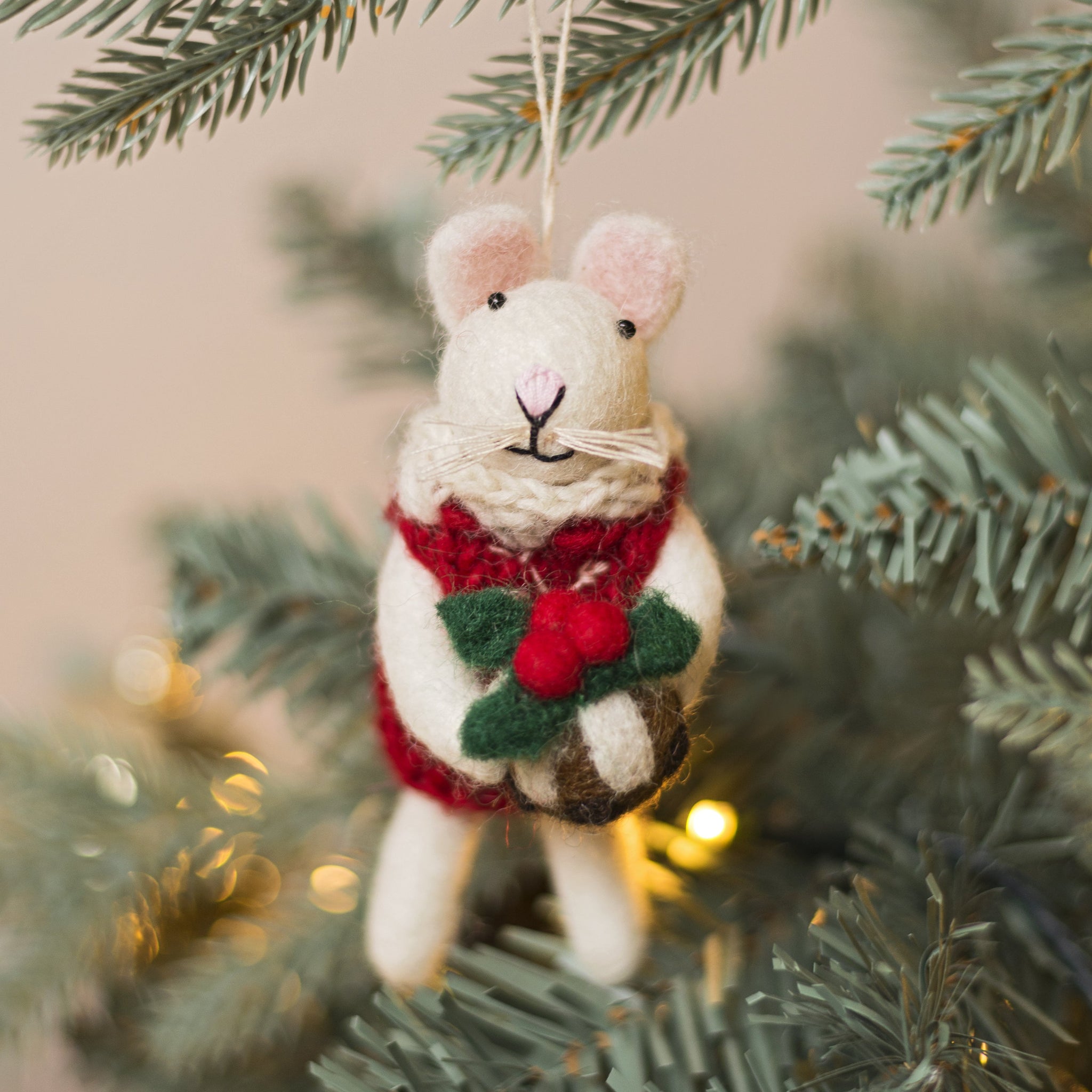 Felt mouse ornament with a red scarf and holly berry hanging on a Christmas tree.