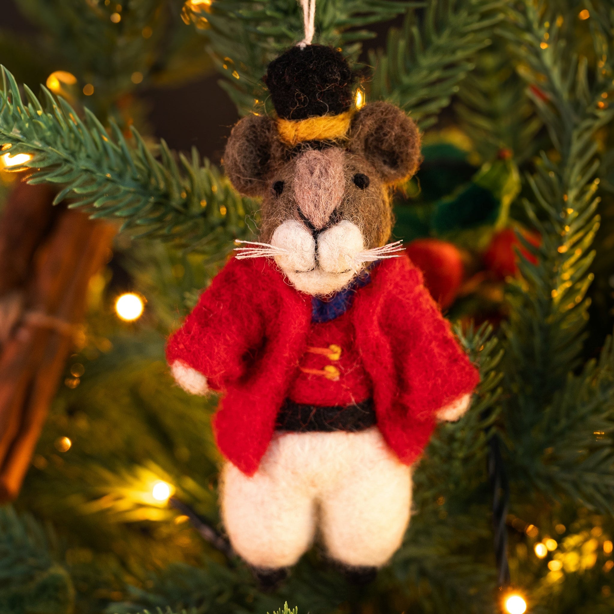 Decorative mouse ornament in a red coat hanging on a Christmas tree.