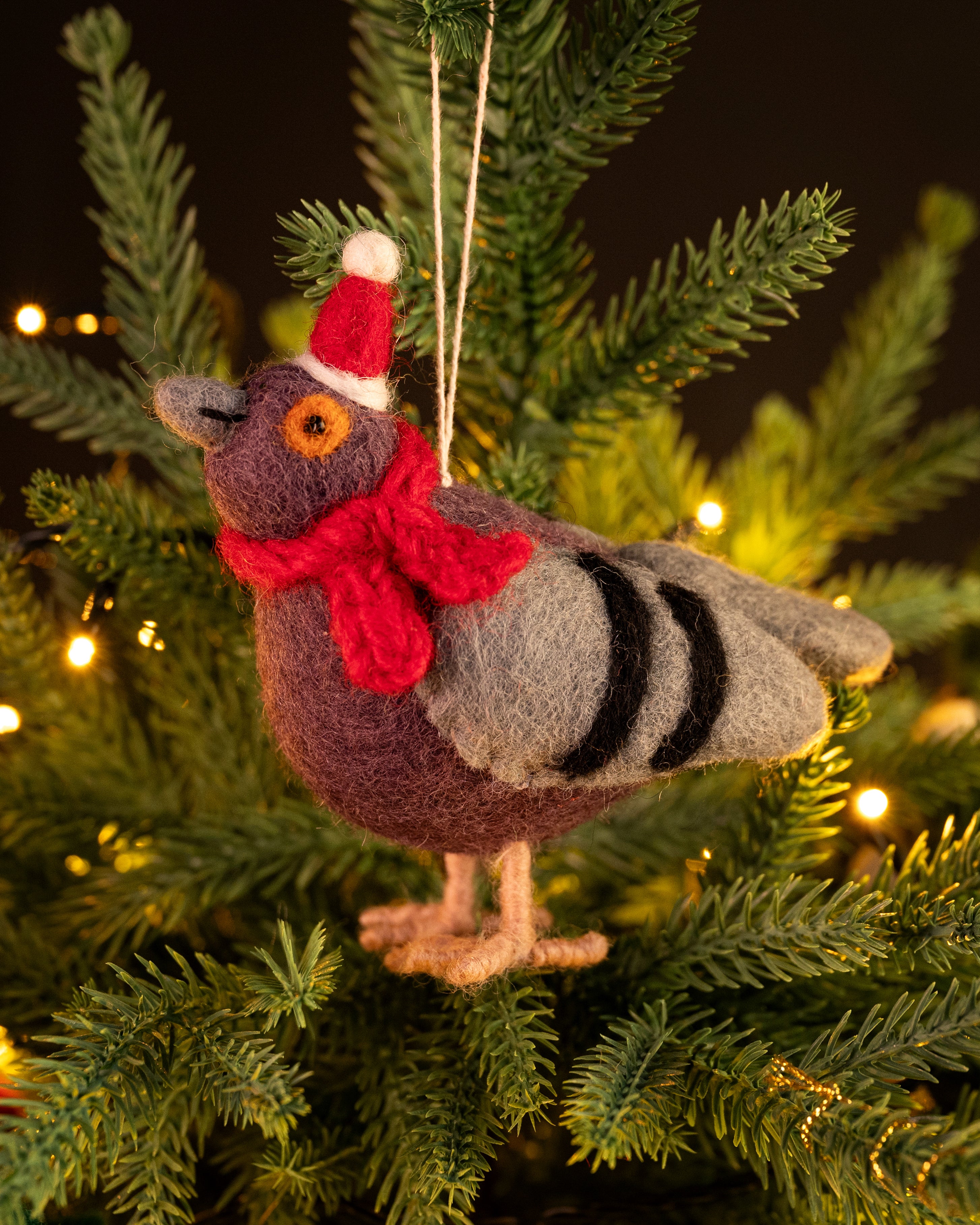 Knitted pigeon ornament with a red scarf and Santa hat on a Christmas tree.