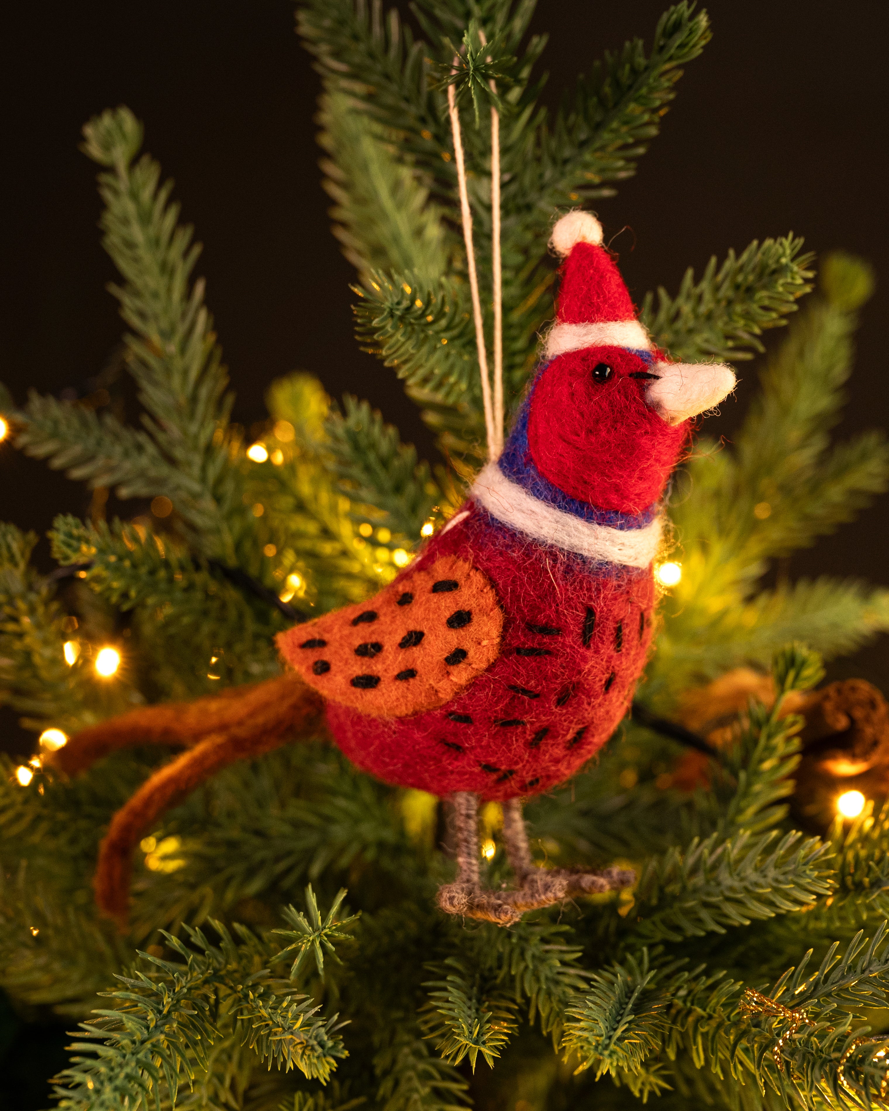 Red and orange bird ornament with a Santa hat hanging on a Christmas tree.