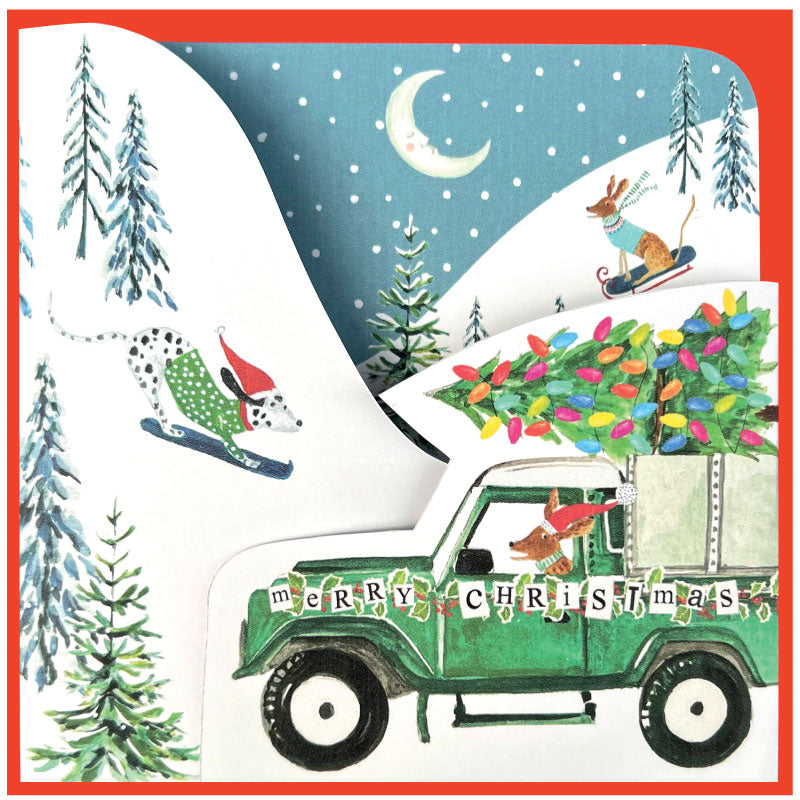 Christmas card with a green truck carrying a Christmas tree, a dog on skis, and a dog on a snowmobile.