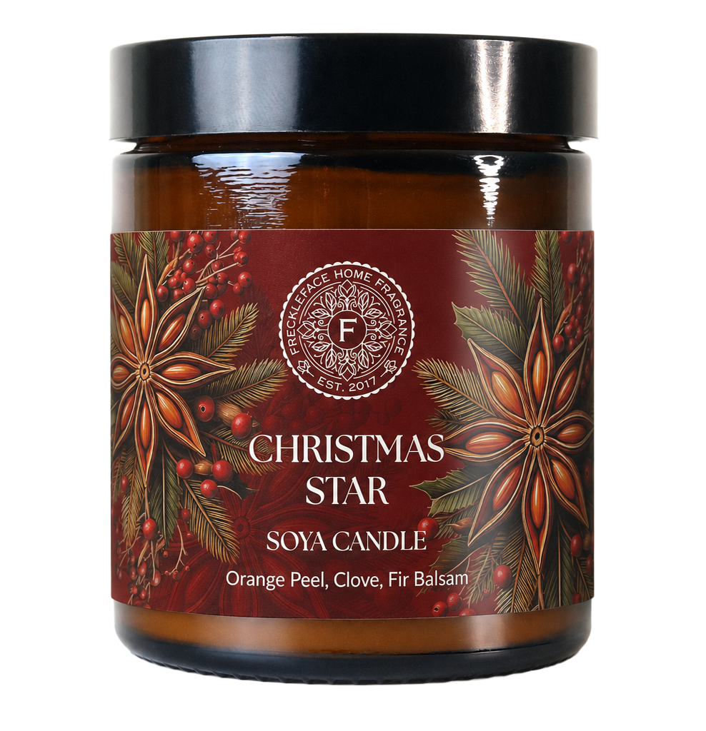 A soy candle in an amber glass jar with a black lid and a dark red holiday label featuring star anise, pine needles, and berries. The label reads 'CHRISTMAS STAR' and 'SOYA CANDLE' with 'Orange Peel, Clove, Fir Balsam' below.
