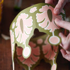 Hand holding a decorative paper cutout with floral patterns on a wooden surface