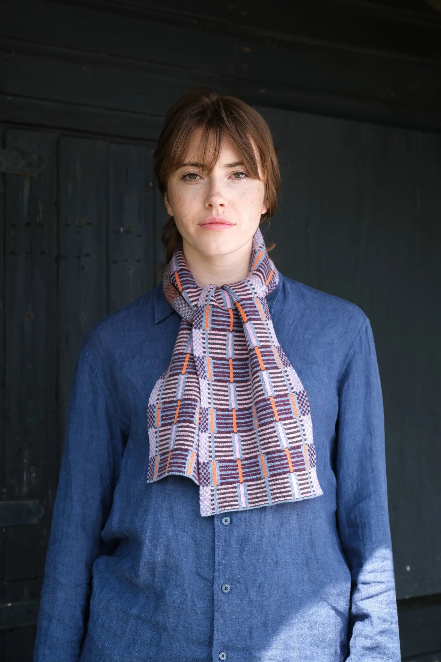 Woman wearing a blue shirt and plaid scarf against a dark background