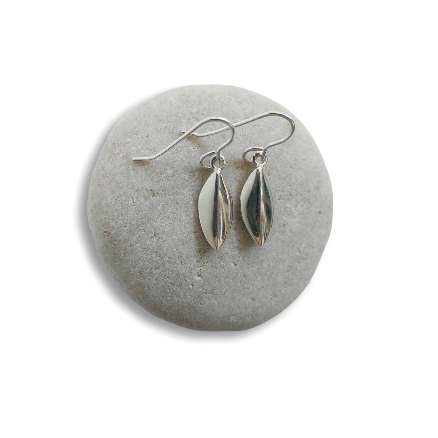 Silver cardamom-shaped earrings on a gray stone surface