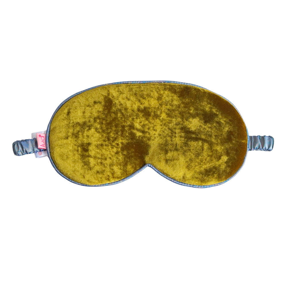 A velvet sleep mask in a mustard yellow color with a blue-gray satin trim and adjustable elastic straps, shown against a plain white background.