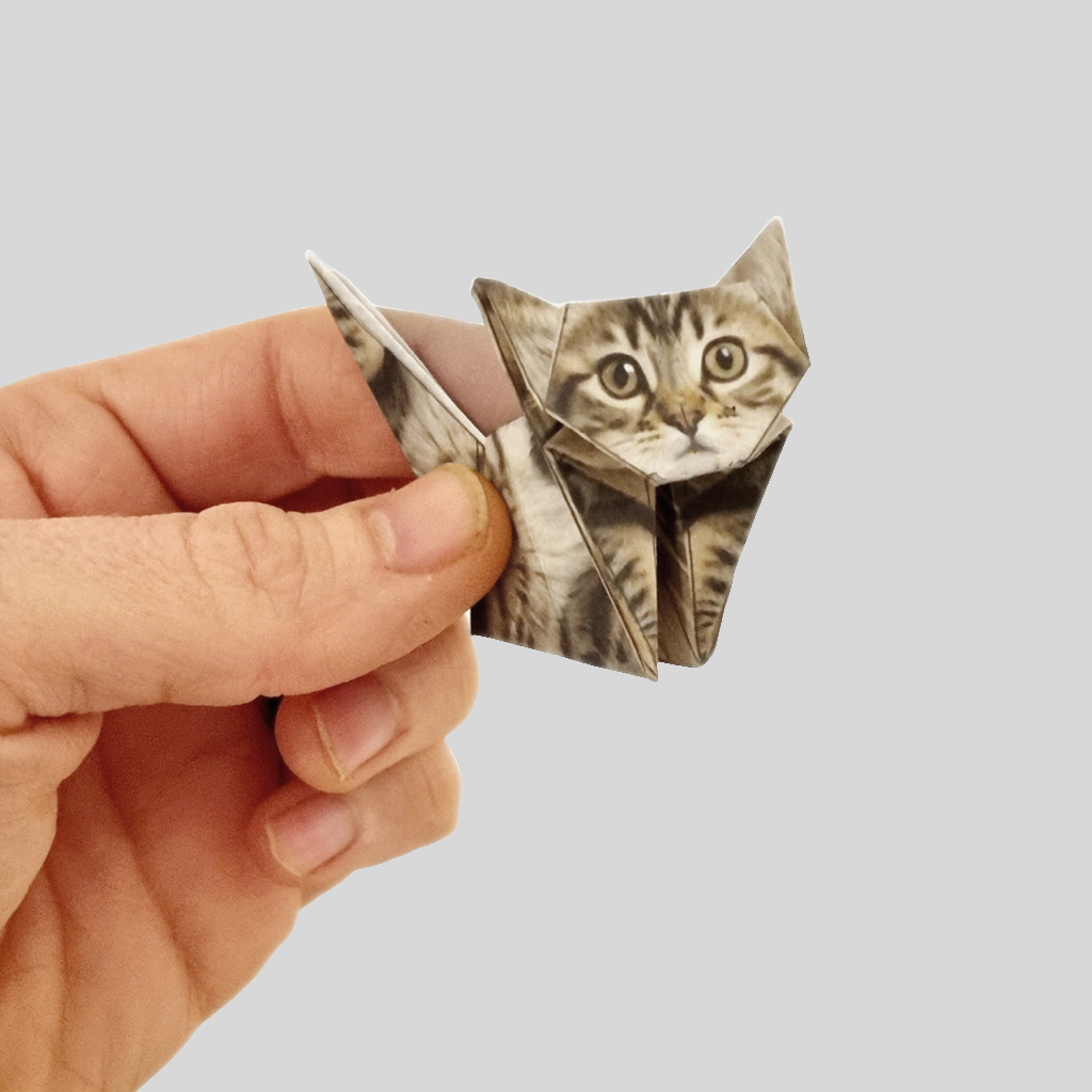 A folded origami cat held in a hand, showing the approximate size of the product.