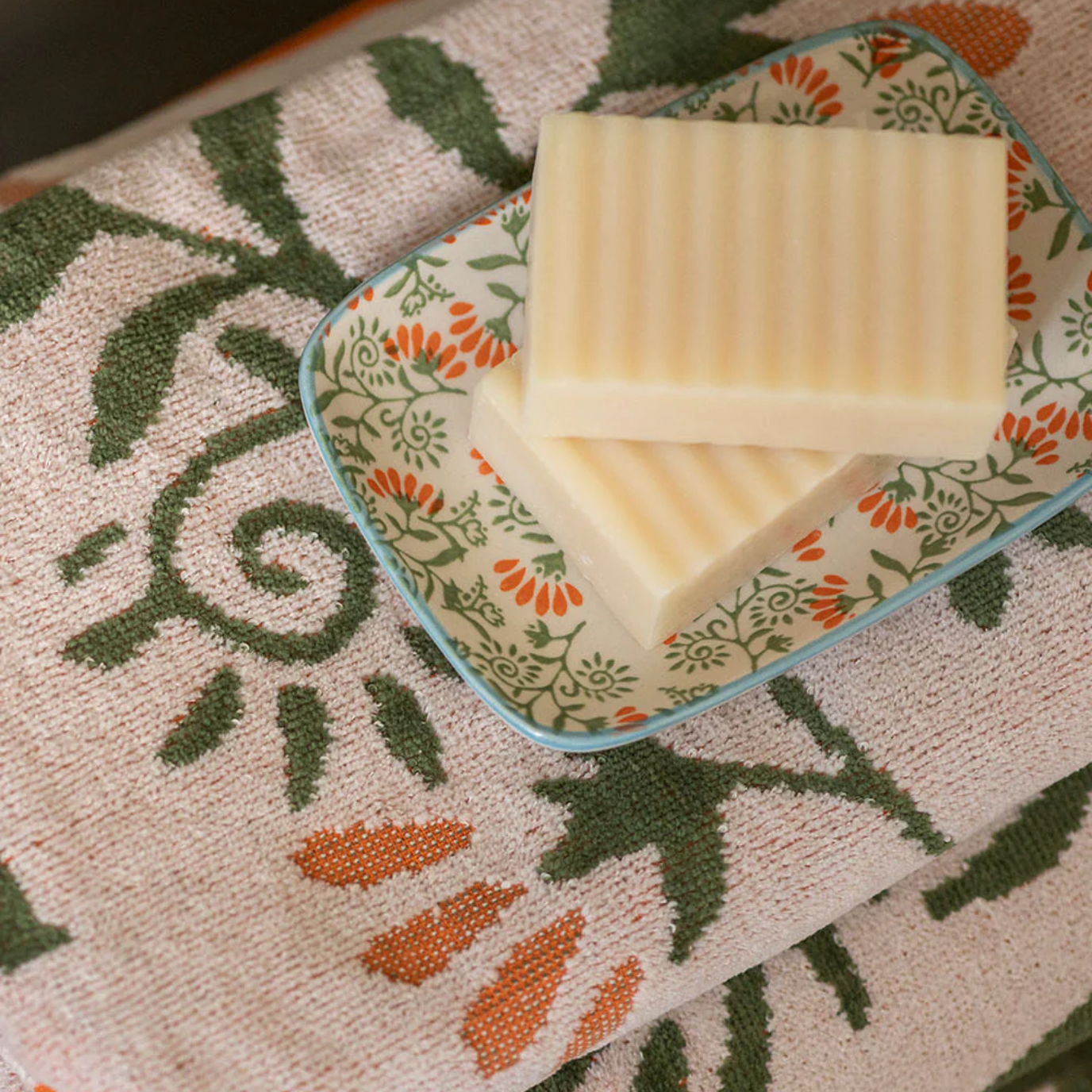 Two bars of soap on a decorative soap dish on a patterned towel