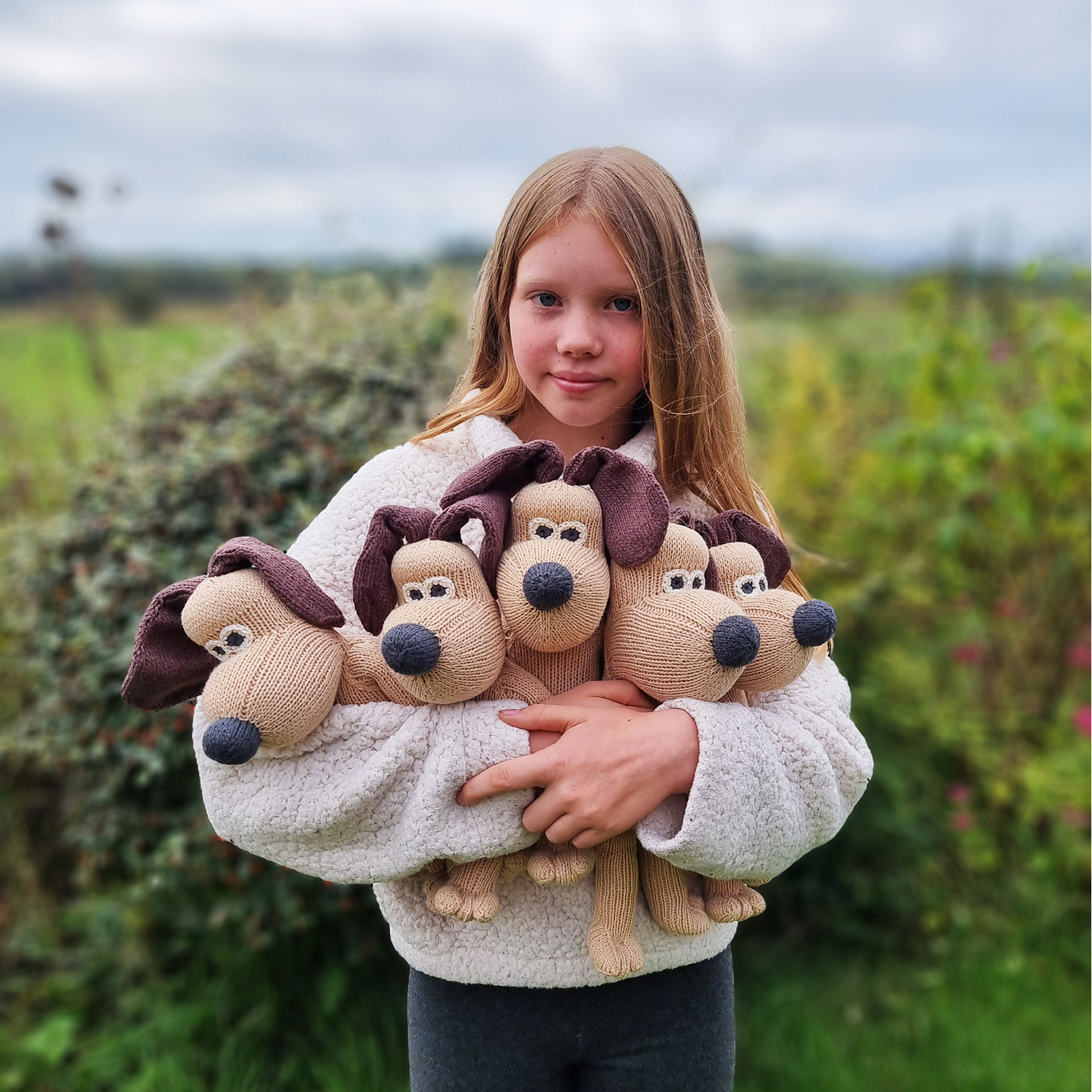 A child standing outdoors in a field holding several plush dog toys.