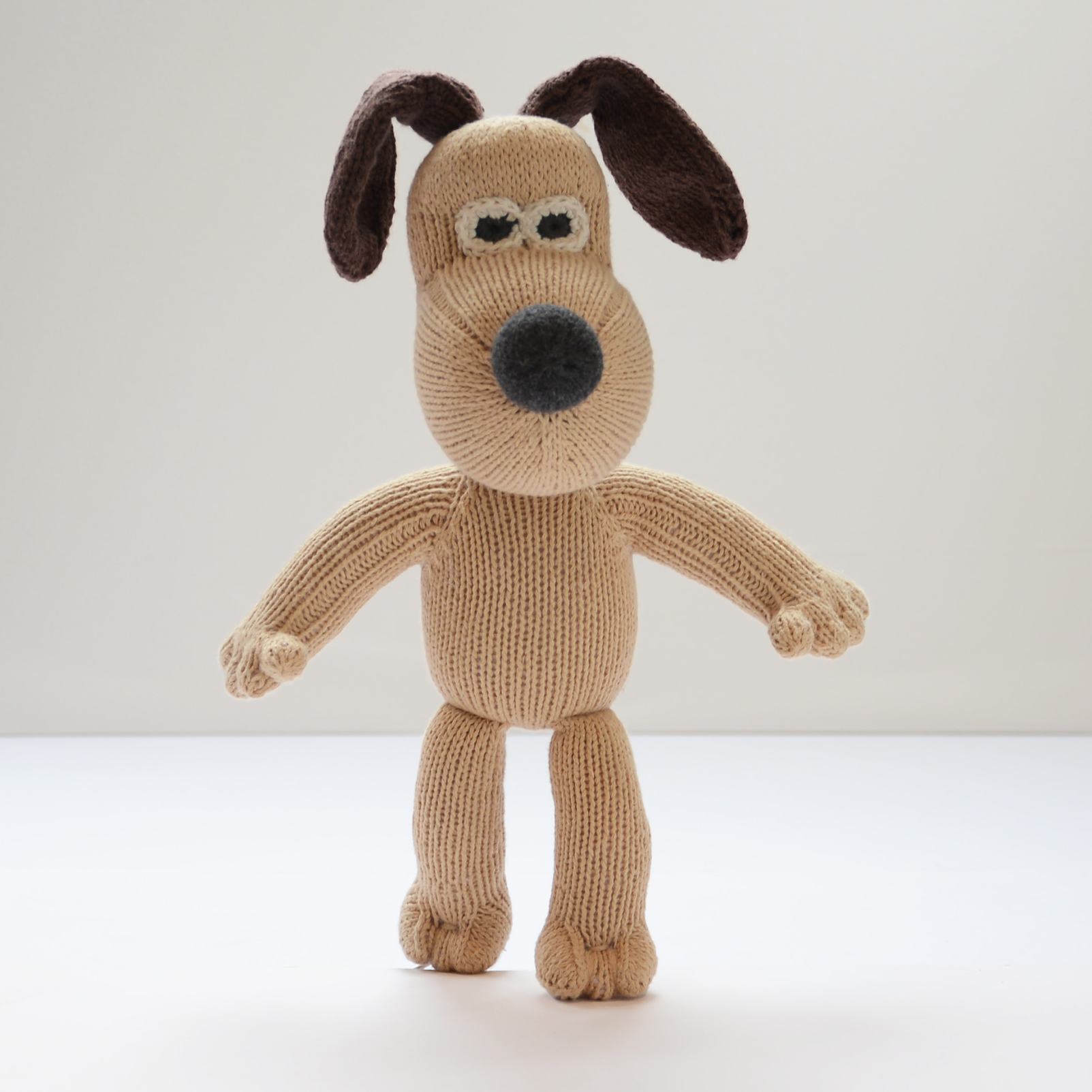 A knitted Gromit-style dog plush toy standing against a plain light background.