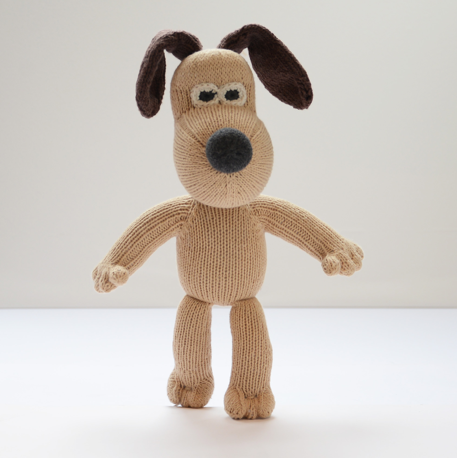 A knitted Gromit-style dog plush toy standing against a plain light background.