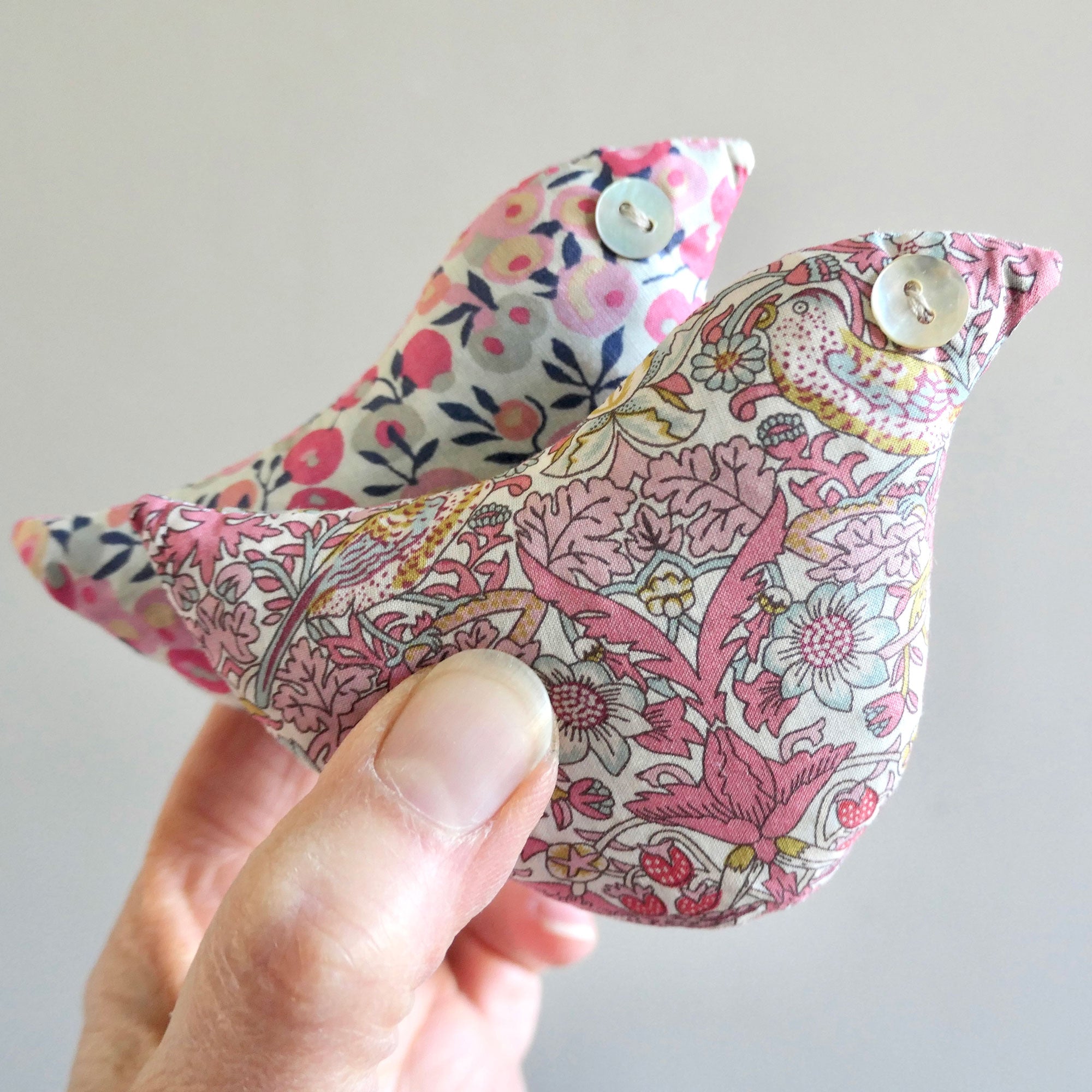 Two fabric birds with floral patterns held by a hand against a light background