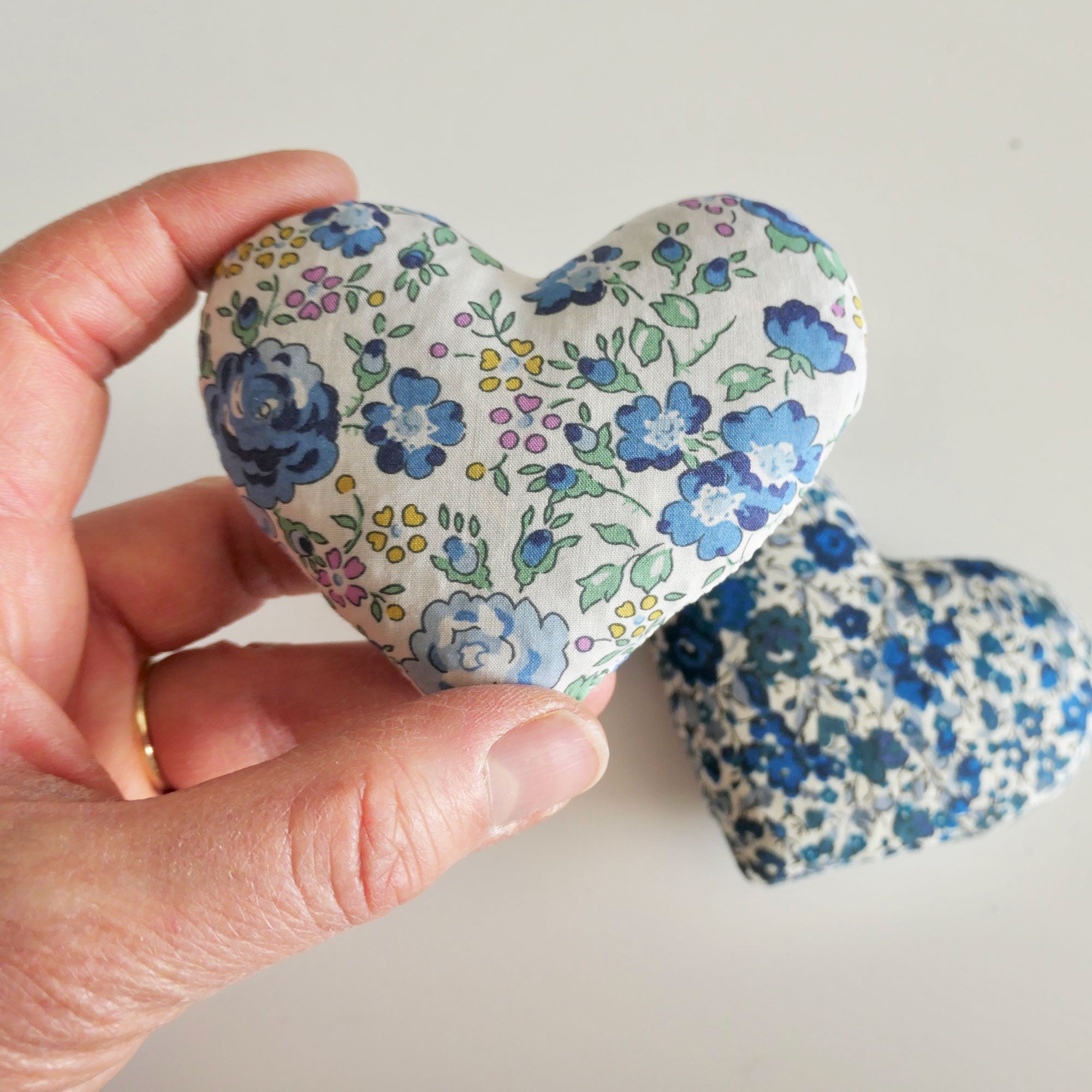 Hand holding a floral-patterned heart-shaped lavender bag against a plain background