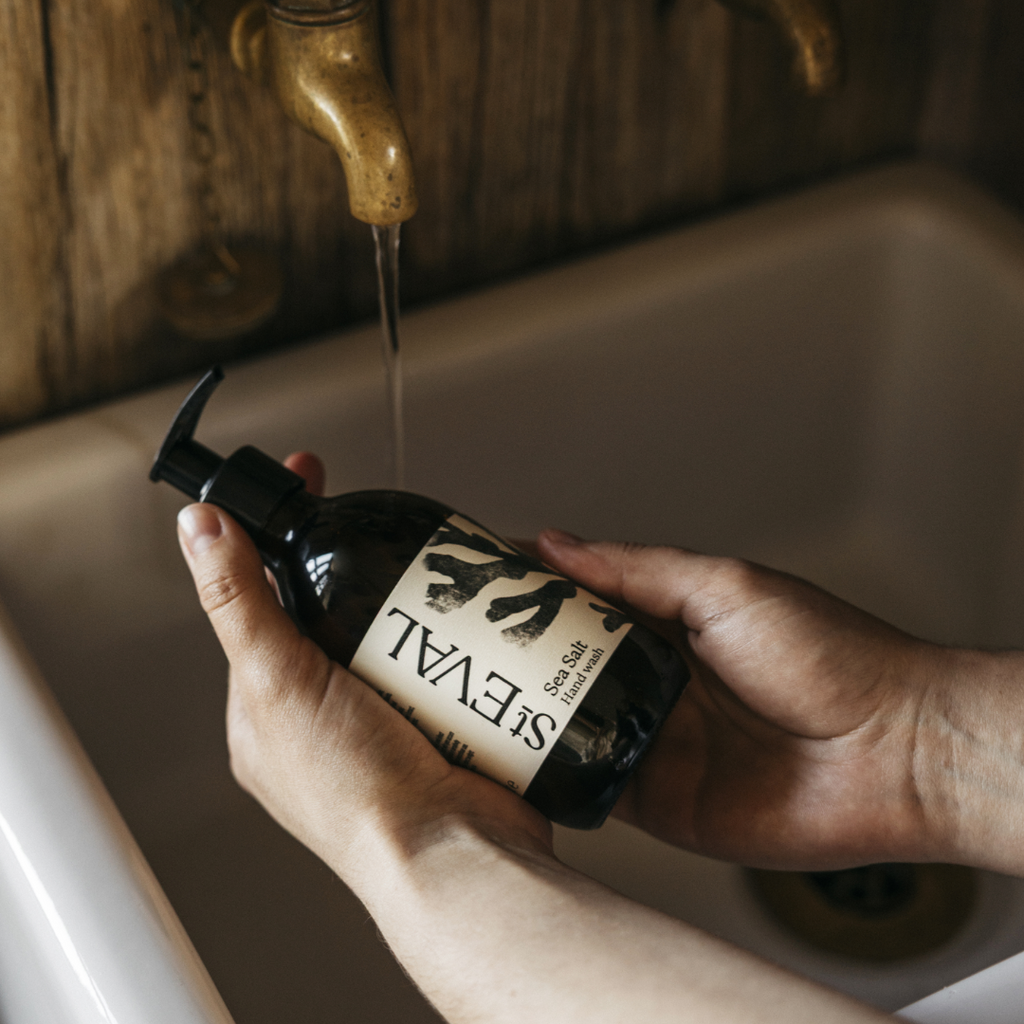 Hands holding bottle of sea salt scented hand wash in a ceramic sink