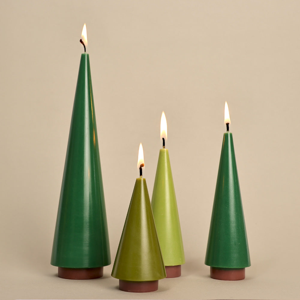 Set of four green tree-shaped candles with flames on a beige background