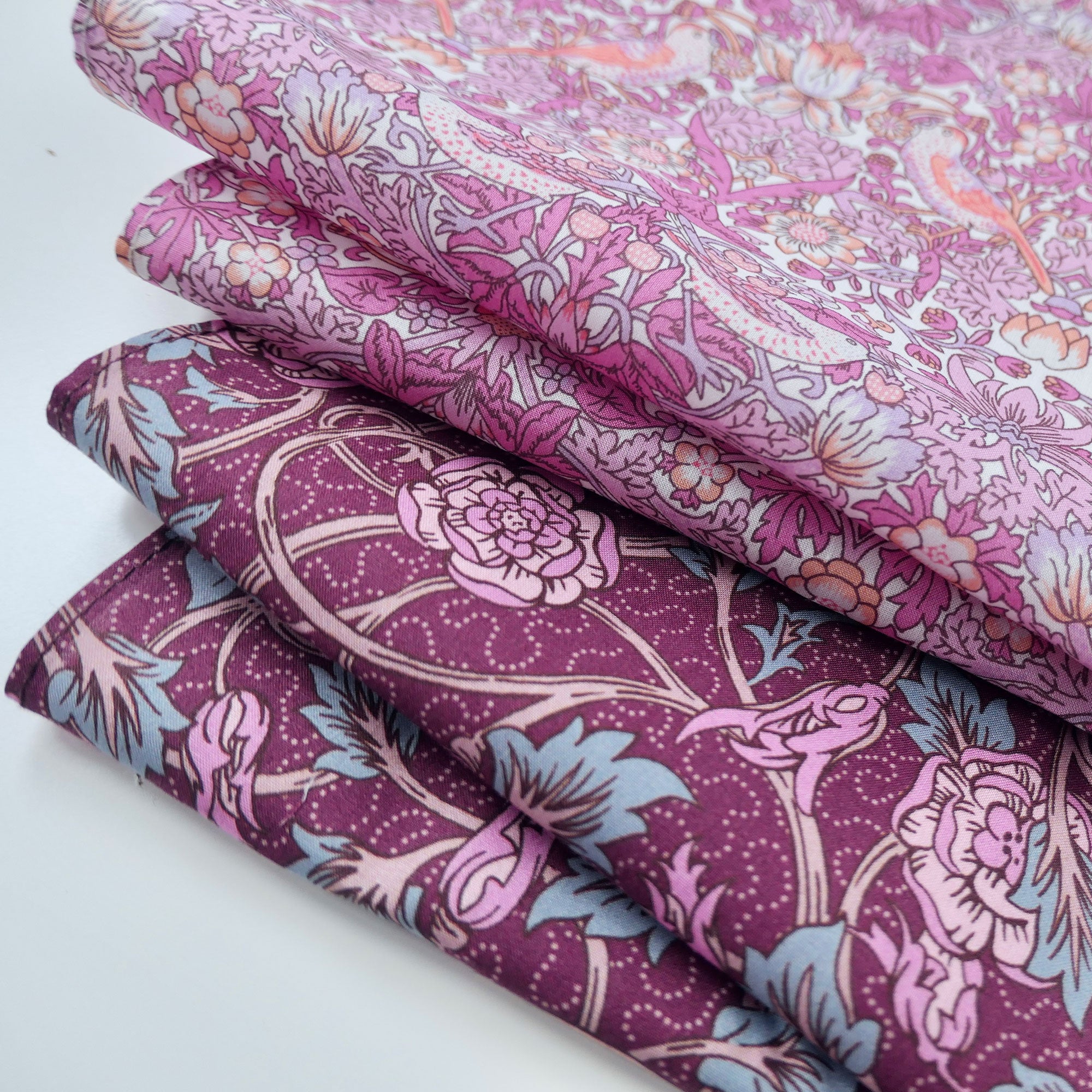 Stack of floral fabric with pink and purple tones on a white background