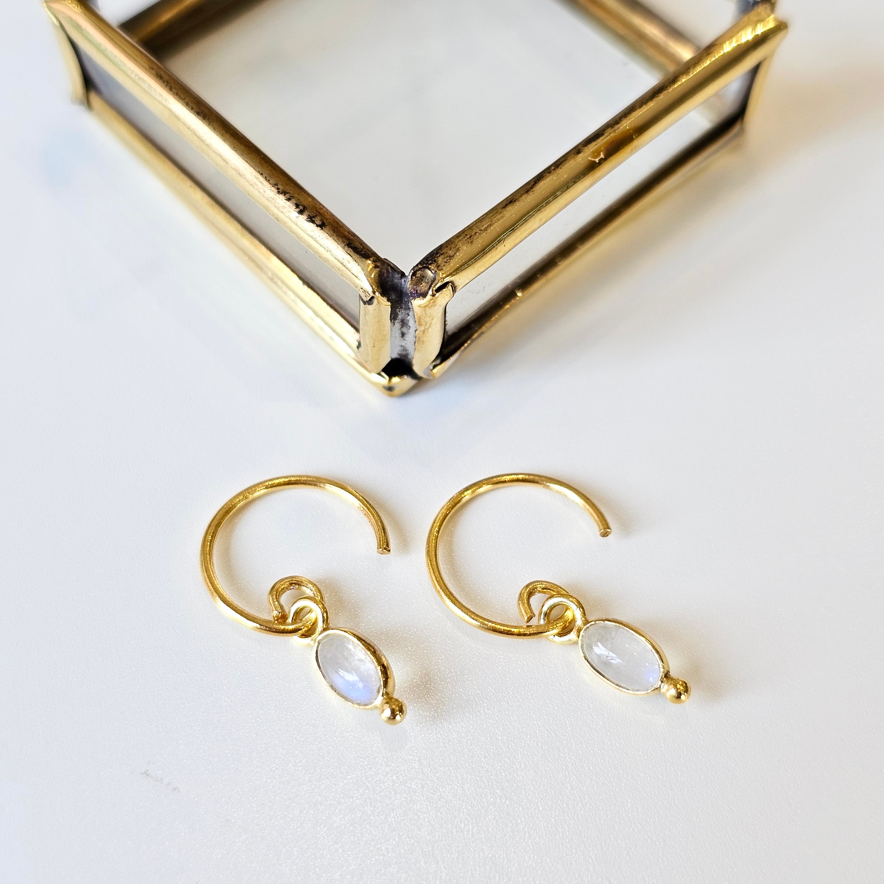 Gold hoop earrings with moonstone drops on a white surface