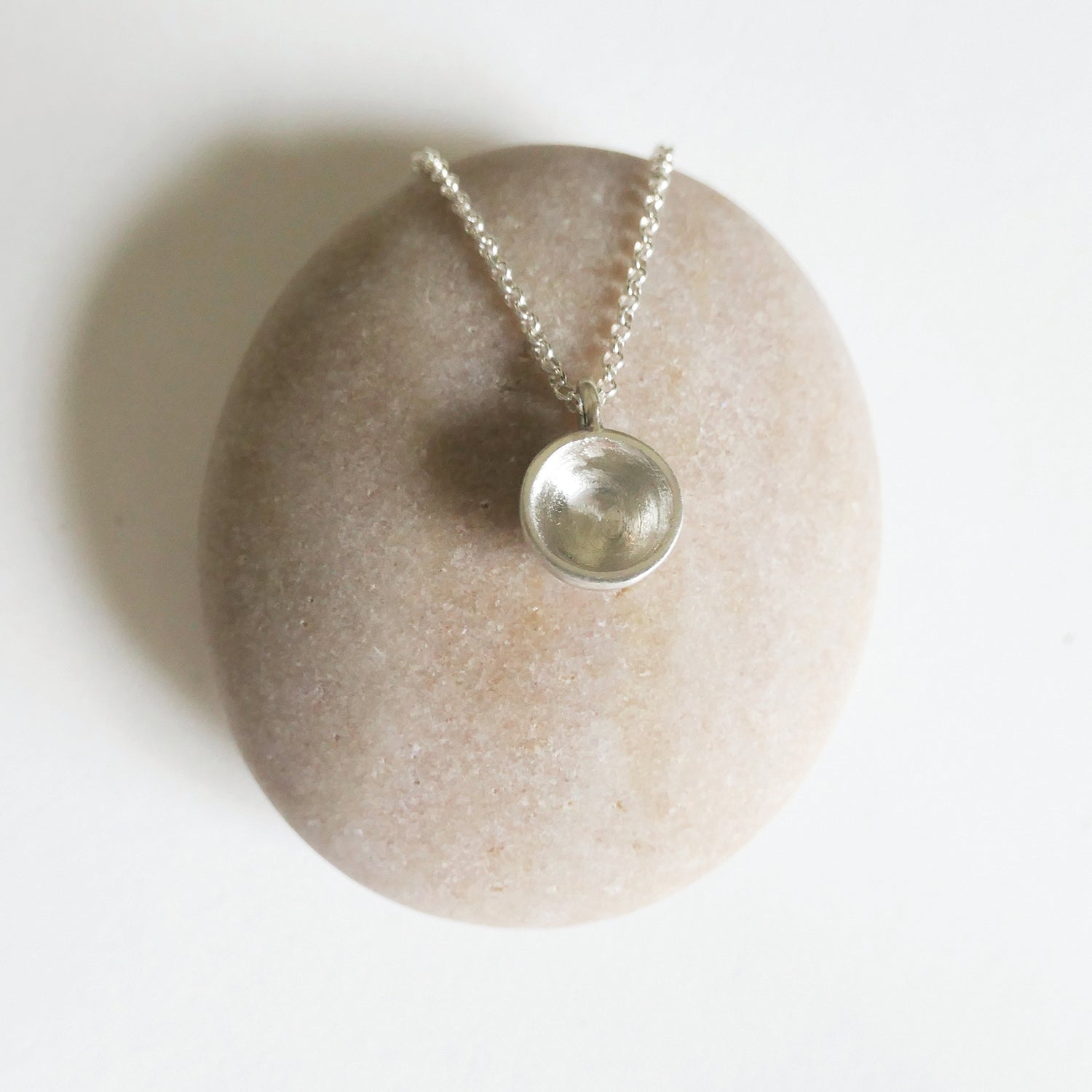 Silver necklace with a round pendant on a beige stone
