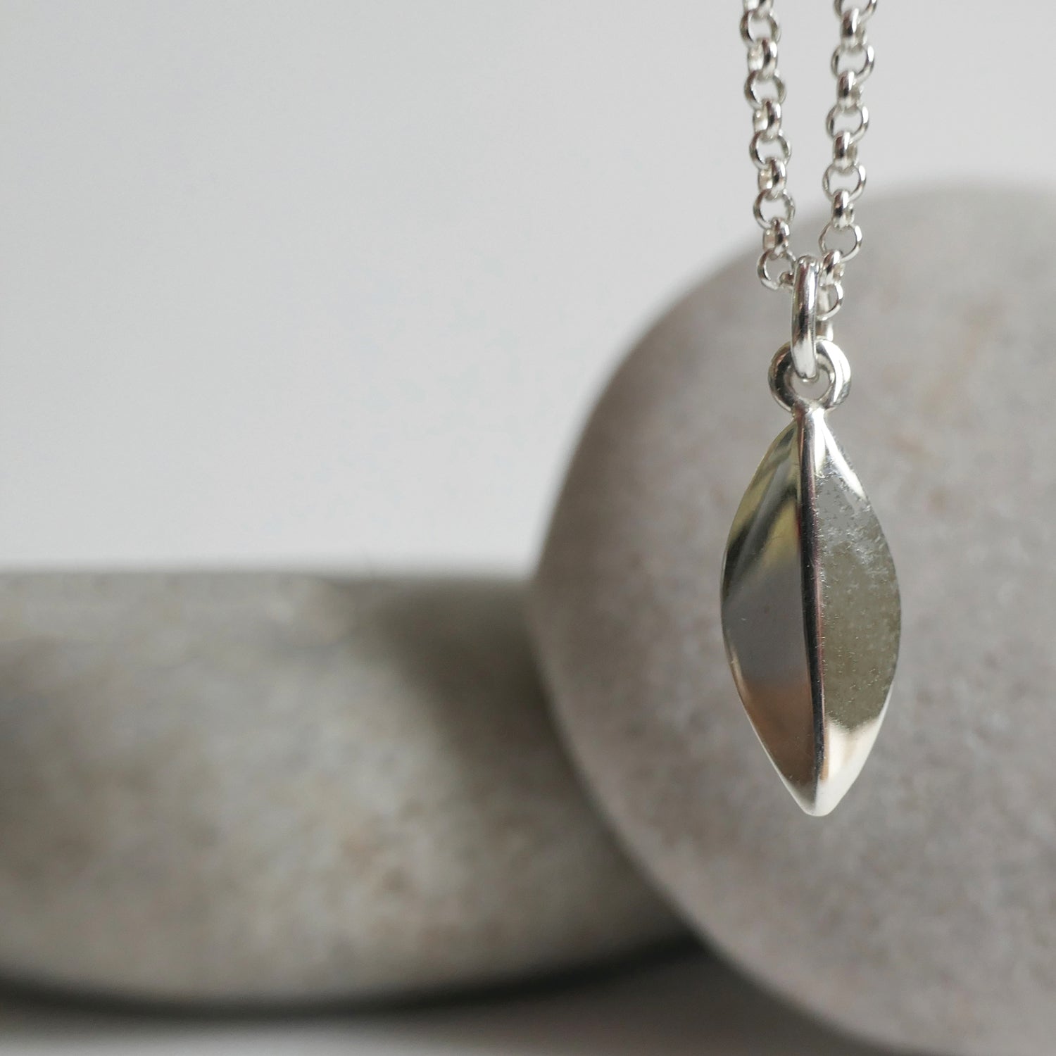 Silver leaf-shaped pendant on a chain against a neutral background