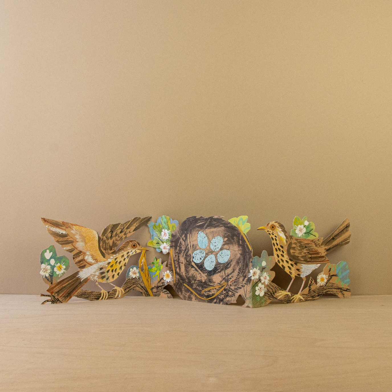Decorative concertina card with birds and flowers on a wooden surface against a beige background