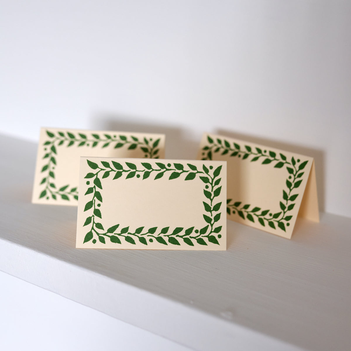 Two beige cards with green leaf patterns on a white surface