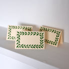 Two beige cards with green leaf patterns on a white surface