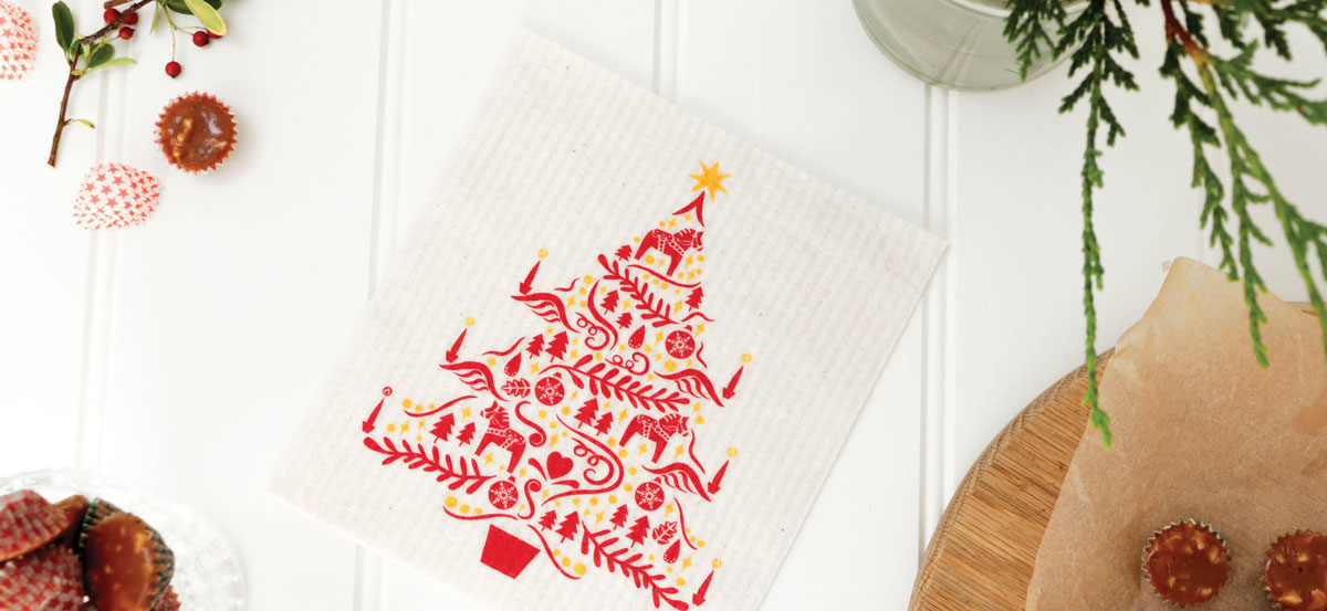 Cloth with red tree design on white surface decorated with greenery and kitchen items