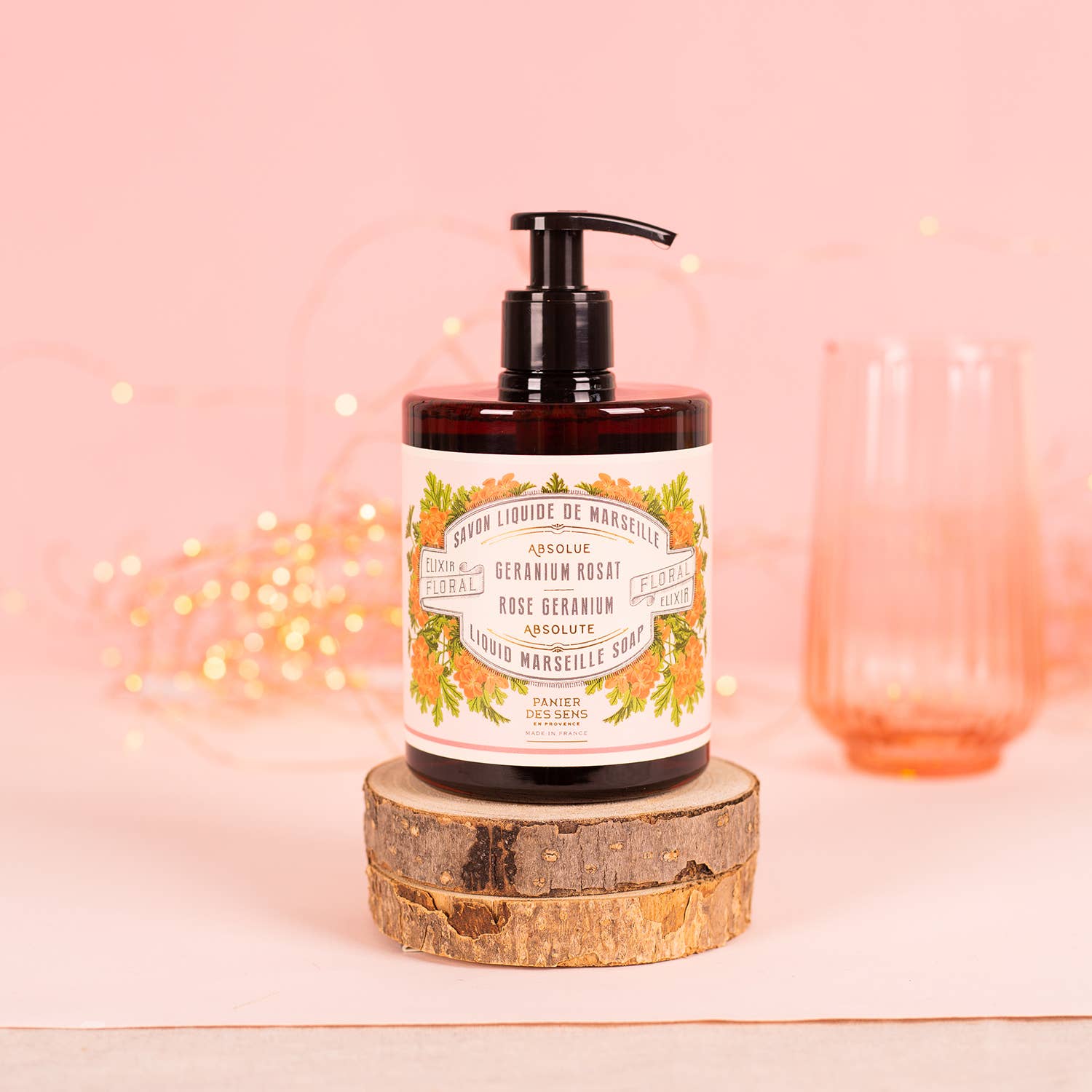 Hand soap bottle with floral label on a wooden block against a pink background