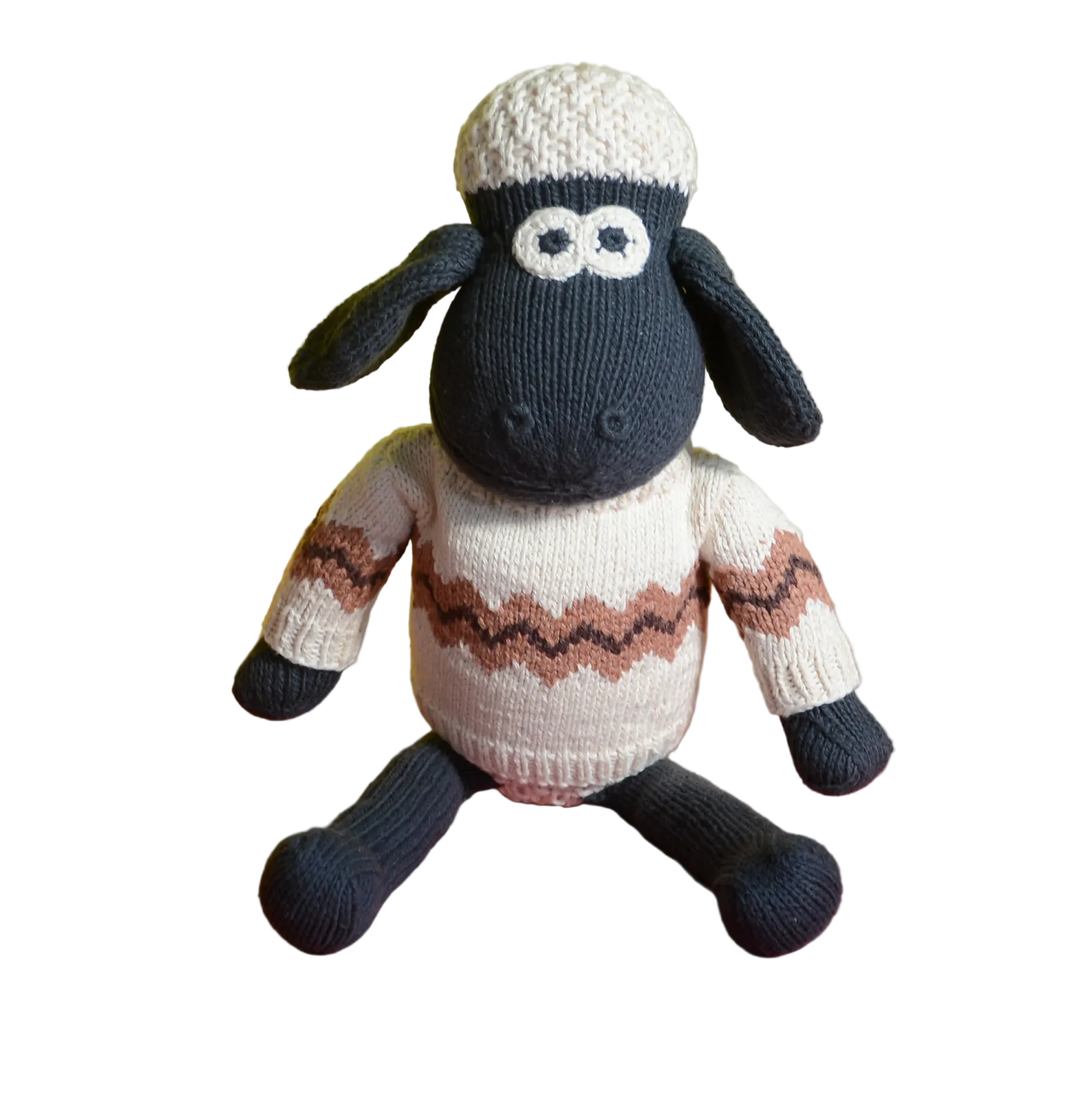 A knitted sheep doll with a black body and face, wearing a cream-coloured sweater with a brown zigzag pattern and a cream knit hat, sitting against a yellow and orange background.