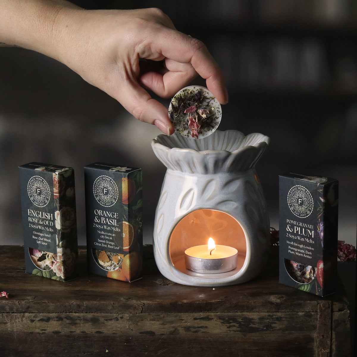 Hand placing a diffuser disc into an oil burner with various diffuser boxes on a wooden surface.
