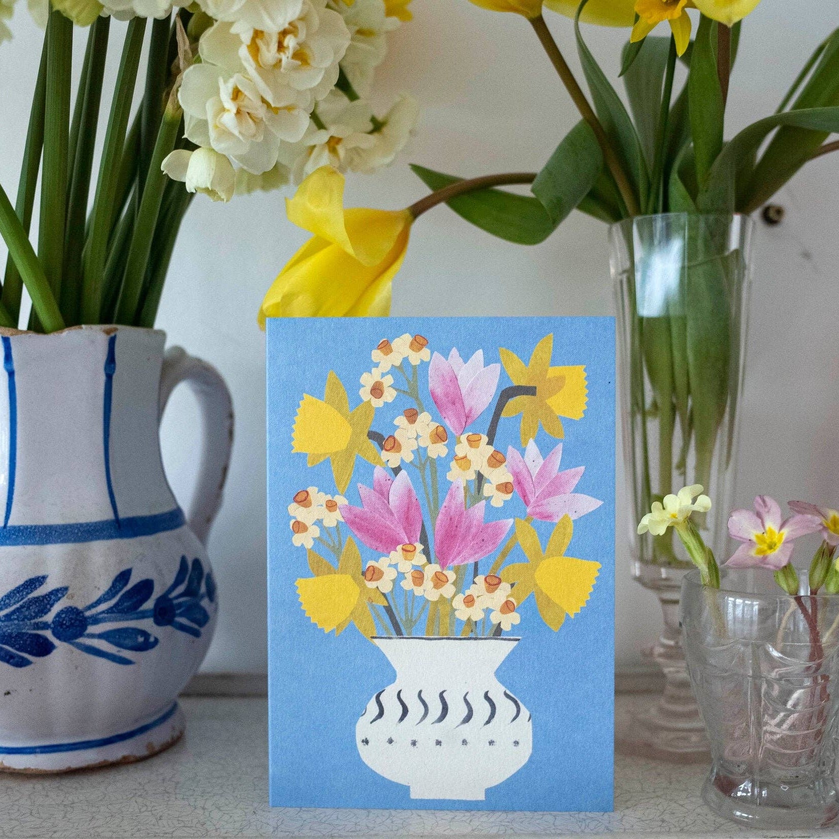 Vases with flowers and a card featuring floral design on a light background