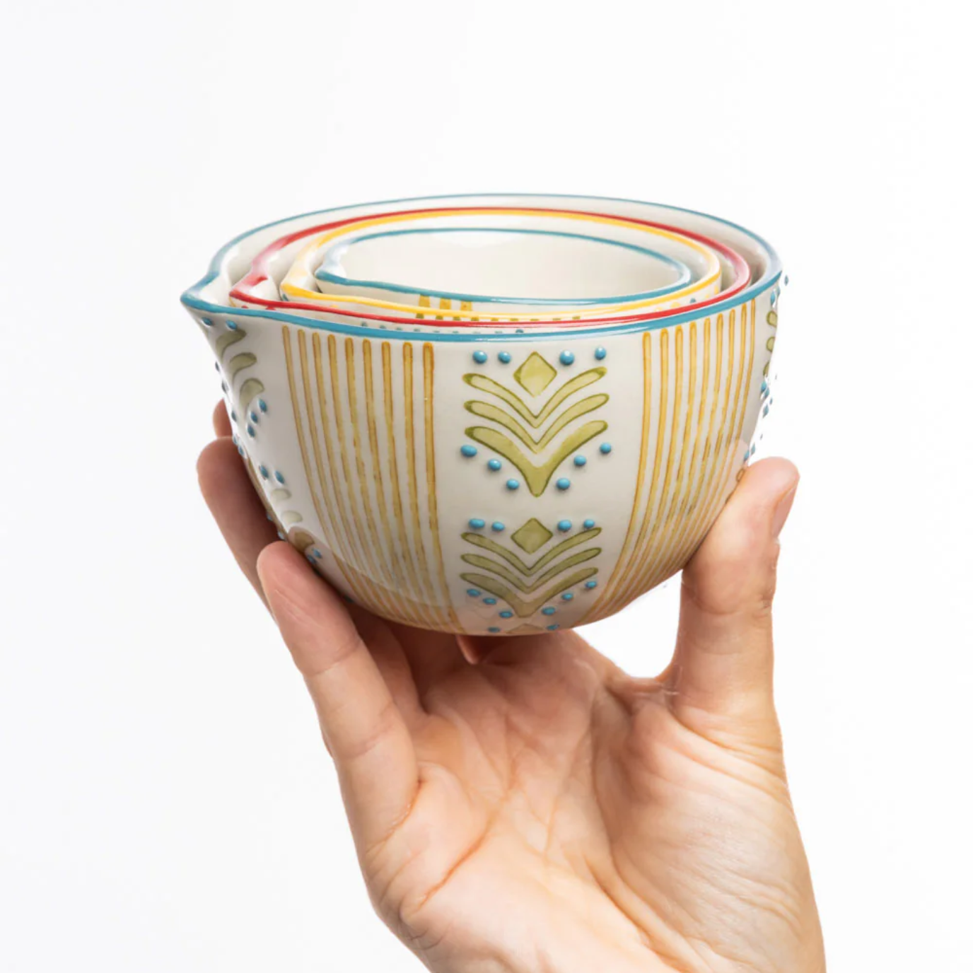 Hand holding a set of stacked ceramic jugs with decorative patterns on a white background