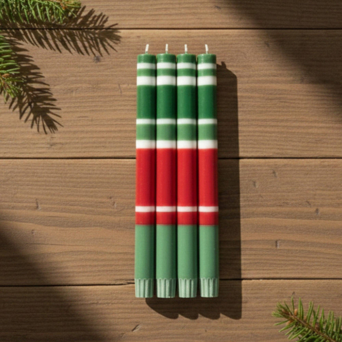 Set of four striped candles in green, red, and white on a wooden surface with pine branches.