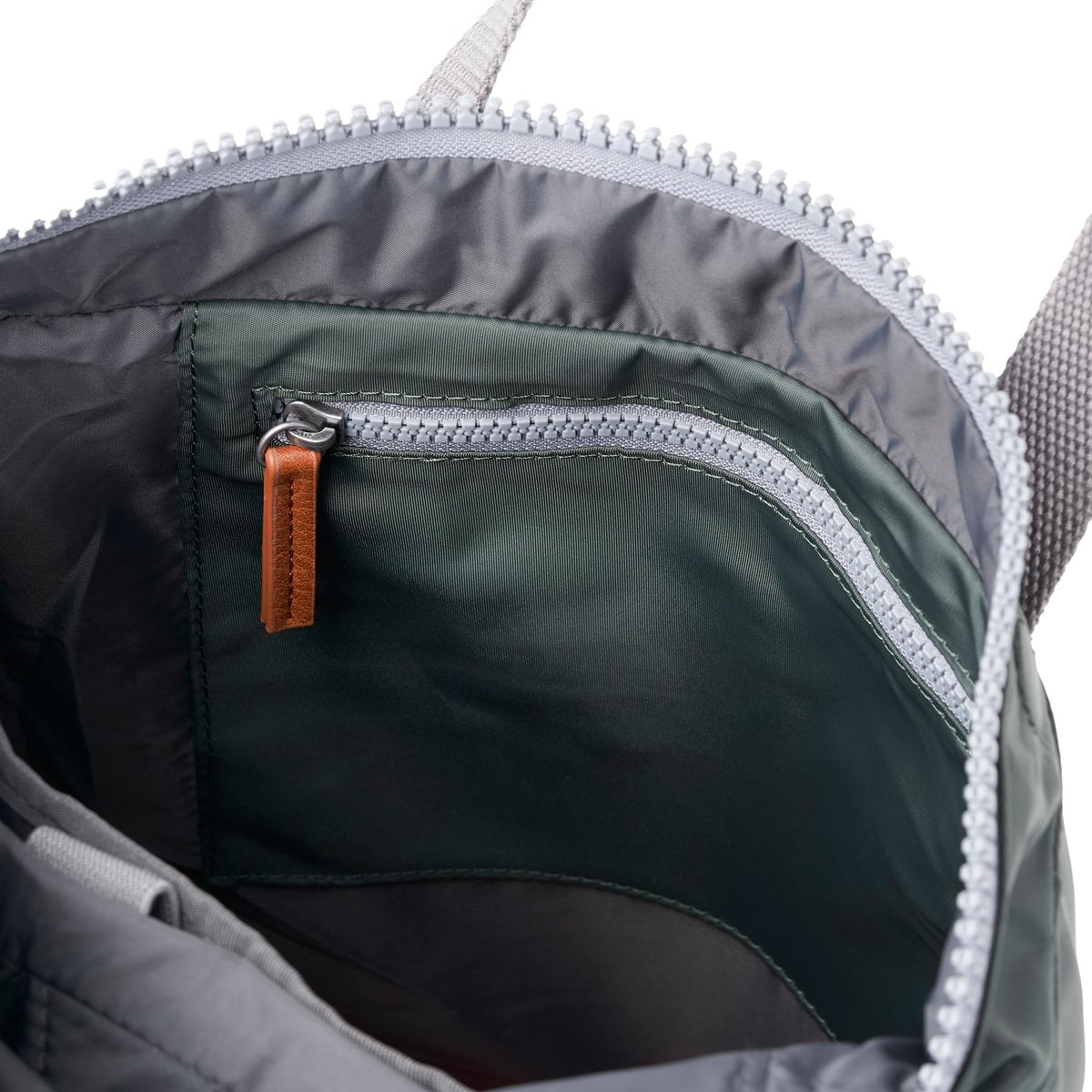 Close-up of a backpack inner zipper pocket with a brown pull tab on a white background