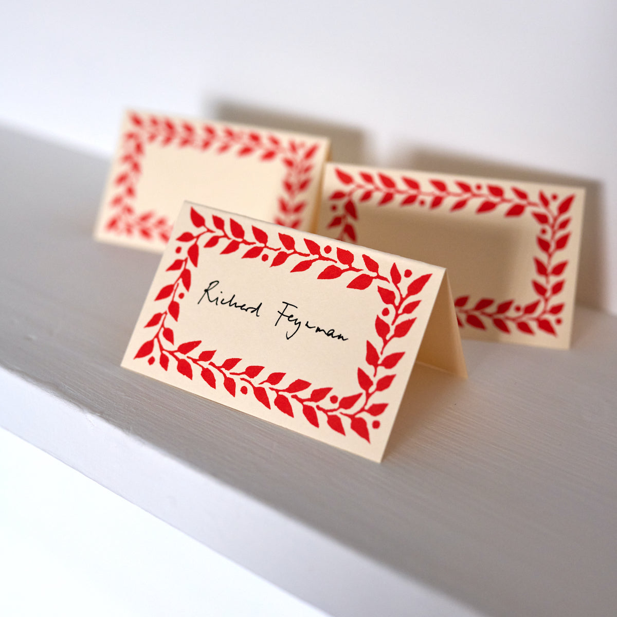 Three place cards with red leaf patterns on a white surface