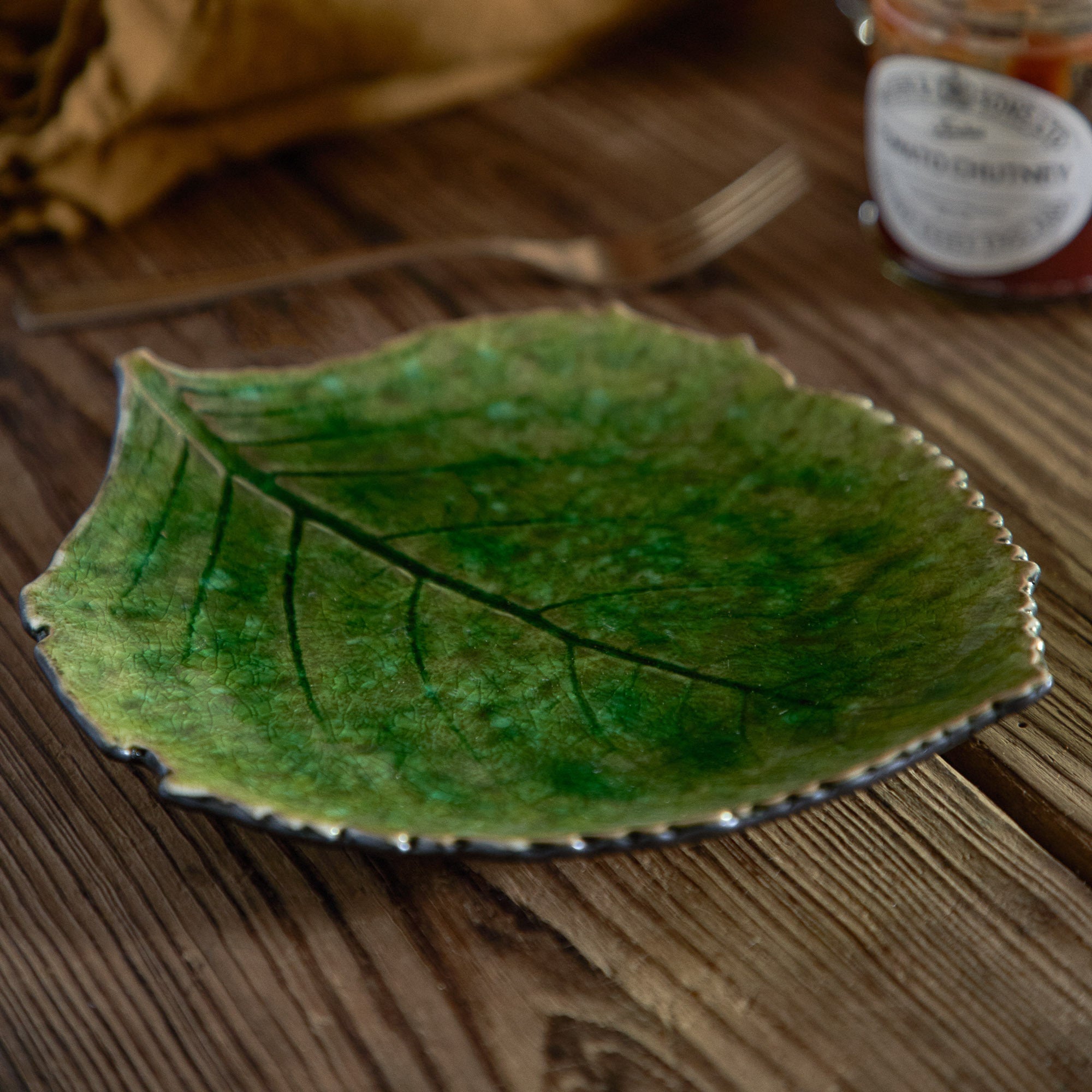 Green leaf-shaped ceramic plate on a wooden surface with a blurred jar in the background.