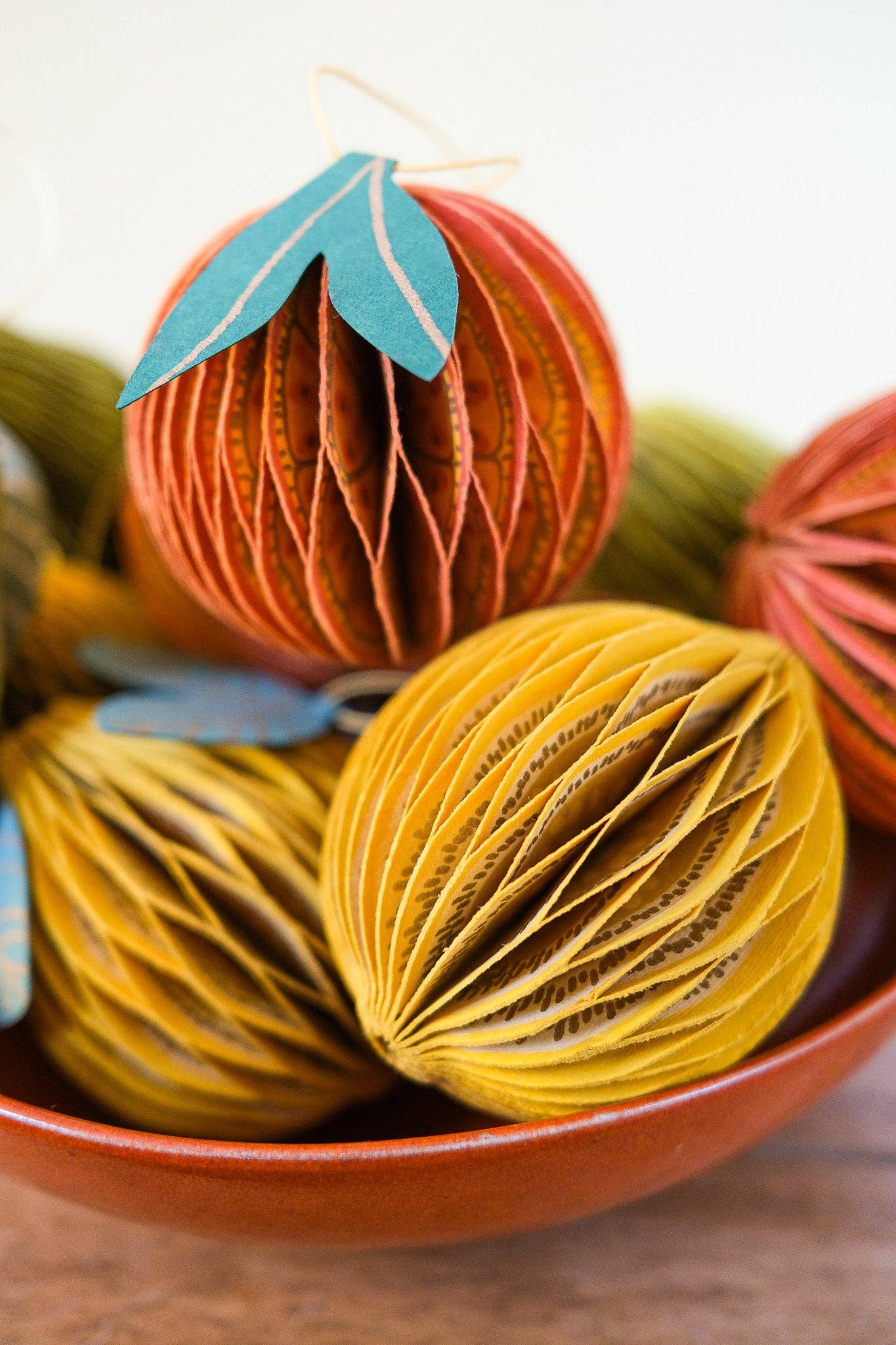 Decorative paper balls in orange and yellow with leaf accents in a bowl.