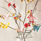 Decorative glass vase with branches, flowers, and colorful paper butterflies on a light background