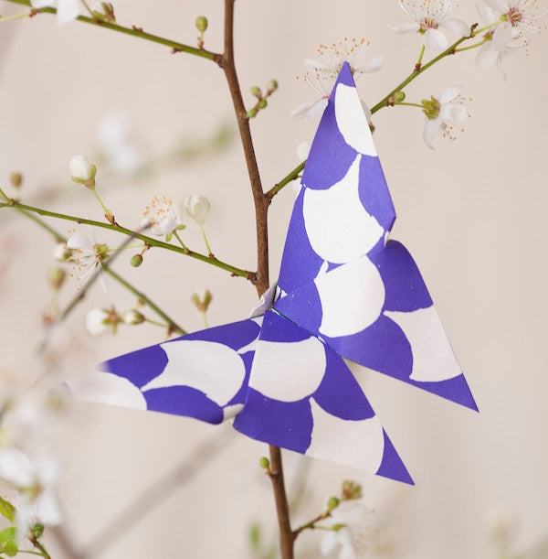 Blue and white patterned paper fish hanging from a branch with white flowers.